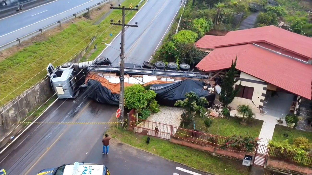 Caminhão tomba na BR-101, sai da pista e atinge residência